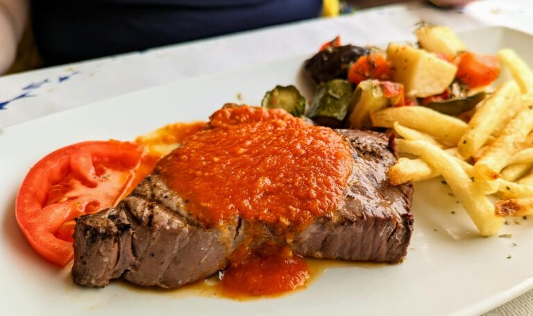 Delicious steak with red sauce, fries, and vegetables on a plate in Agia Galini.