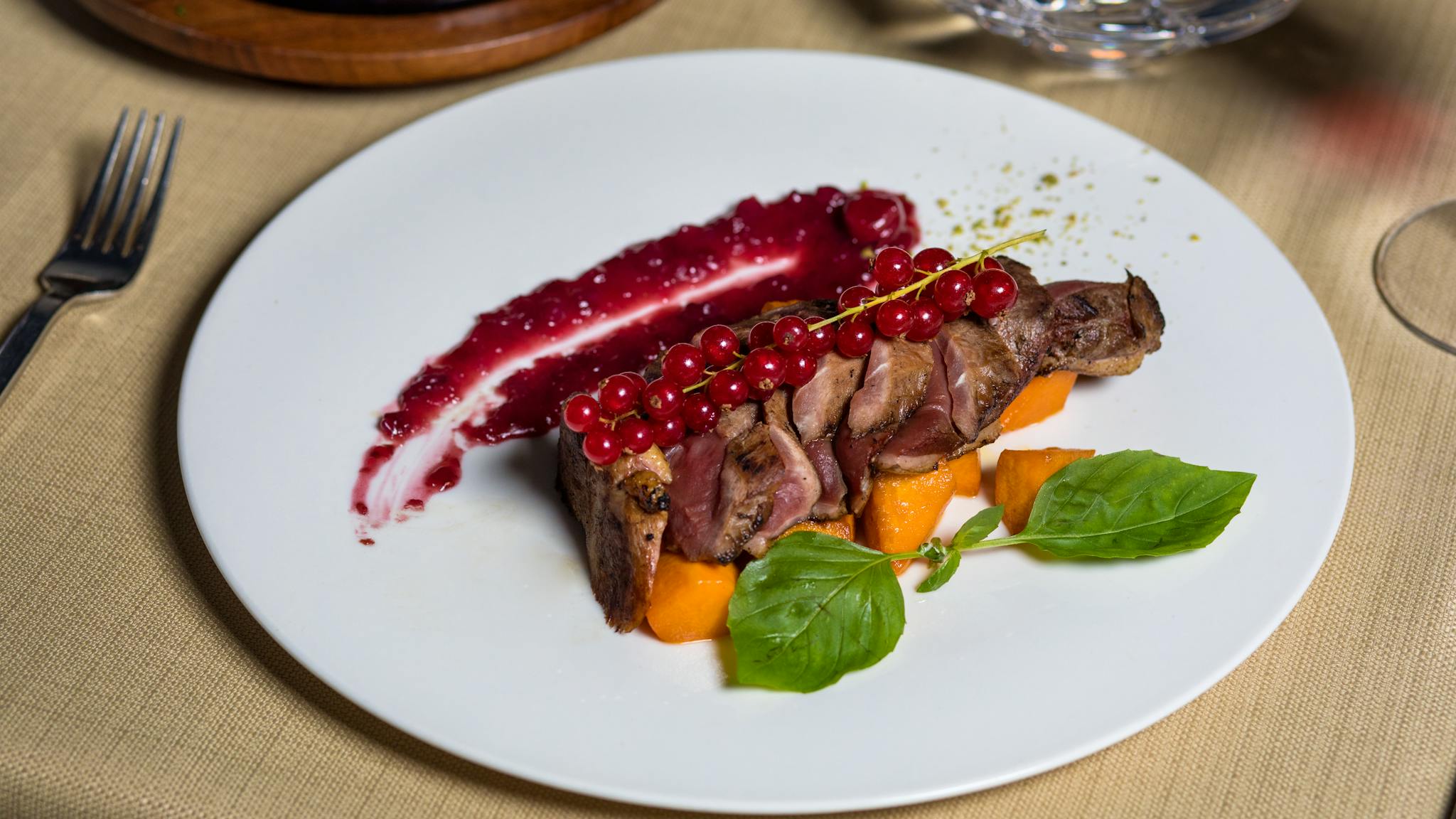 Elegant plated duck breast with berry sauce, garnished with herbs and vegetables, perfect for gourmet dining.